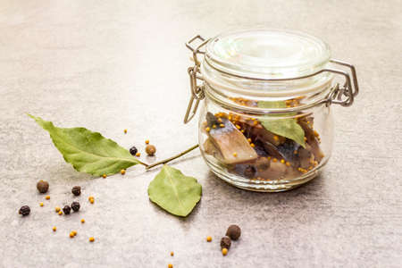 Slices of herring with spices in a glass jar. Mustard seeds, bay leaf, pepper mix. Healthy traditional food concept. Stone background, close upの写真素材