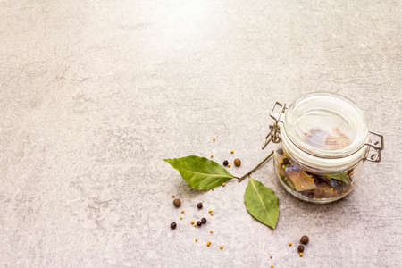 Slices of herring with spices in a glass jar. Mustard seeds, bay leaf, pepper mix. Healthy traditional food concept. Stone background, copy spaceの写真素材