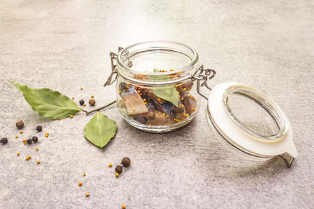 Slices of herring with spices in a glass jar. Mustard seeds, bay leaf, pepper mix. Healthy traditional food concept. Stone background, close upの写真素材