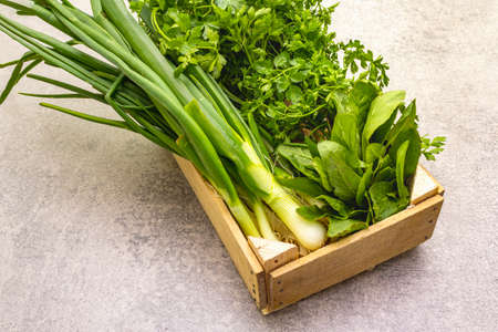 A bunch of fresh green onions, sorrel and parsley in wooden box. Healthy vegetarian (vegan) food concept, ingredients for cooking. On a stone background, close upの写真素材