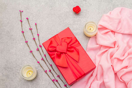 Romantic gift concept. Red box with bow, candles, artificial flowers, cloth. On a stone background, top viewの写真素材