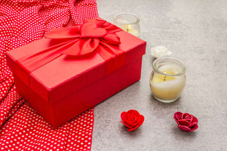 Romantic gift concept. Red box with bow, candles, artificial flowers, polka dot cloth. On a stone background, copy spaceの写真素材