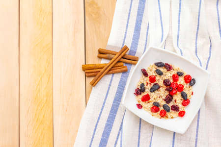 Healthy vegetarian (vegan) breakfast with oatmeal and fruits. Dried berries and cinnamon sticks with a vintage linen napkin on a wooden background, top view, copy spaceの写真素材