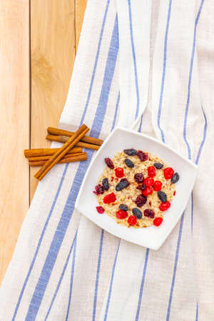 Healthy vegetarian (vegan) breakfast with oatmeal and fruits. Dried berries and cinnamon sticks with a vintage linen napkin on a wooden background, top viewの写真素材