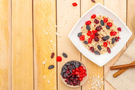 Healthy vegetarian (vegan) breakfast with oatmeal and fruits. Dried berries and cinnamon sticks with a vintage linen napkin on a wooden background, top viewの写真素材