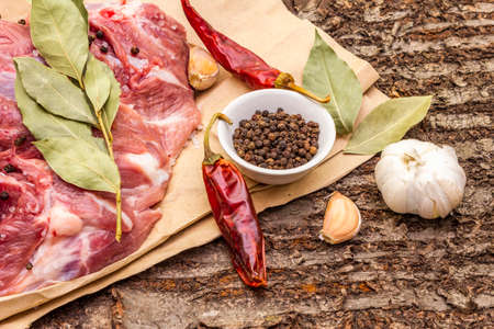 Raw pork shoulder with spices. Bay leaf, garlic, chili. On a wooden bark background, close upの写真素材