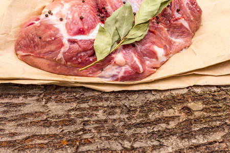 Raw pork shoulder with black pepper and bay leaf. On a wooden bark background, close up, copy spaceの写真素材