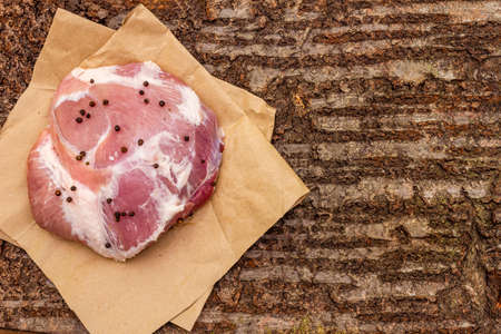 Raw pork shoulder with black pepper. On a wooden bark background, close up, copy space, top viewの写真素材