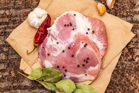 Raw pork shoulder with spices. Bay leaf, garlic, chili. On a wooden bark background, close up, top viewの写真素材