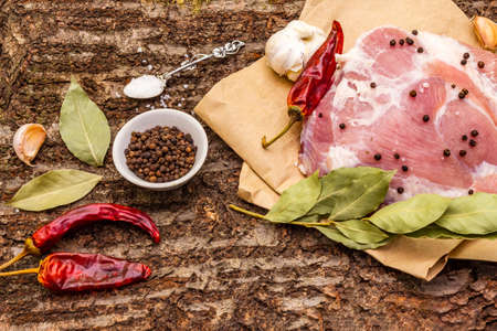 Raw pork shoulder with spices. Bay leaf, garlic, chili. On a wooden bark background, close upの写真素材