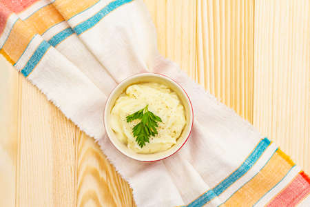 Warm mashed potatoes in a ceramic bowl with fresh parsley. On a vintage linen napkin on a wooden background, top view, copy space, close upの写真素材