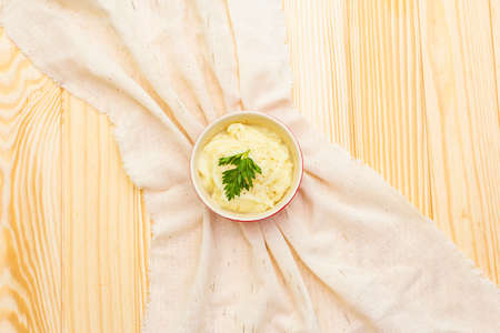 Warm mashed potatoes in a ceramic bowl with fresh parsley. On a vintage linen napkin on a wooden background, top view, copy spaceの写真素材