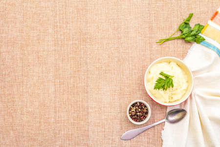 Warm mashed potatoes in a ceramic bowl with fresh parsley and dry pepper mix. On a linen cloth background, copy space, top viewの写真素材