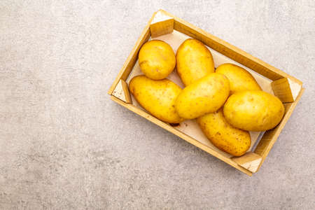 Raw unpeeled young potatoes in a wooden crate. New harvest, on stone background, copy space, top viewの写真素材