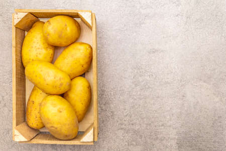Raw unpeeled young potatoes in a wooden crate. New harvest, on stone background, copy space, top viewの写真素材
