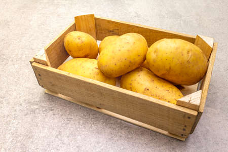 Raw unpeeled young potatoes in a wooden crate. New harvest, on stone background, close upの写真素材