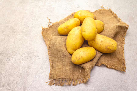 Raw unpeeled young potatoes on sackcloth. New harvest, heap on a stone background, close upの写真素材