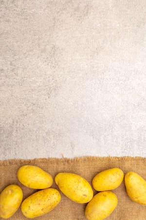 Raw unpeeled young potatoes on sackcloth. New harvest, heap on a stone background, top view, copy spaceの写真素材