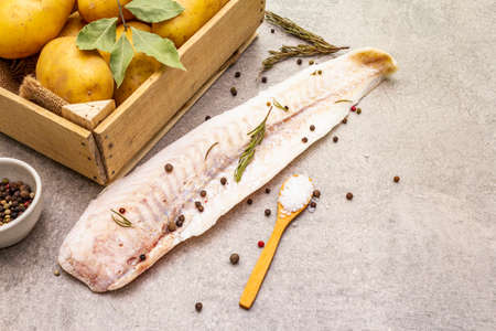 Raw young potatoes and frozen hake fillets. Ingredients for fish and chips. Spices and herbs on a stone background, copy space, close upの写真素材