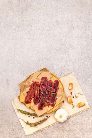 Basturma, dried tenderloin of beef meat, jerky, thinly sliced. Dry rosemary, pepper mix, chili, garlic on vintage linen cloth. Delicious food on a wooden board, stone background, copy space, top viewの写真素材