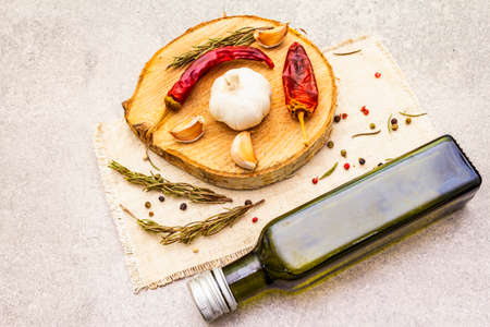 Traditional Italian cooking background. Garlic, rosemary, hot chili pepper, pepper mix, olive oil. Dry spices and herbs on wooden board and vintage linen cloth. Stone backgroundの写真素材