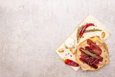 Basturma, dried tenderloin of beef meat, jerky, thinly sliced. Dry rosemary, pepper mix, chili, garlic on vintage linen cloth. Delicious food on a wooden board, stone background, copy space, top viewの写真素材