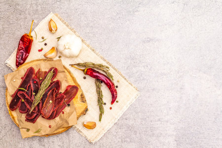 Basturma, dried tenderloin of beef meat, jerky, thinly sliced. Dry rosemary, pepper mix, chili, garlic on vintage linen cloth. Delicious food on a wooden board, stone background, copy space, top viewの写真素材