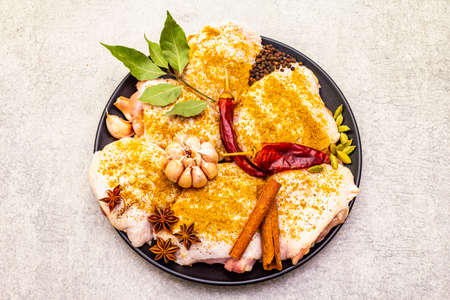 Raw chicken thighs with traditional indian spices. Yellow curry mix, star anise, cardamom, bay leaf, pepper, garlic, cinnamon. Ingredients for cooking on a stone background, close up, top viewの写真素材