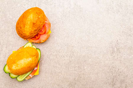 Homemade sandwich in bun. Salami, dried pork, tomato, cucumber, cheese ingredients. On stone...