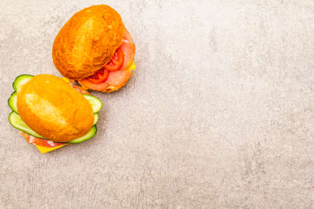 Homemade sandwich in bun. Salami, dried pork, tomato, cucumber, cheese ingredients. On stone background, top viewの写真素材