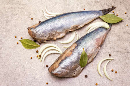 Traditional Norwegian herring "Matias Queen", whole carcasses. Ingredient for smorrebrod, snacks, antipasti. With sliced onion, black pepper, coriander. On stone background, close upの写真素材