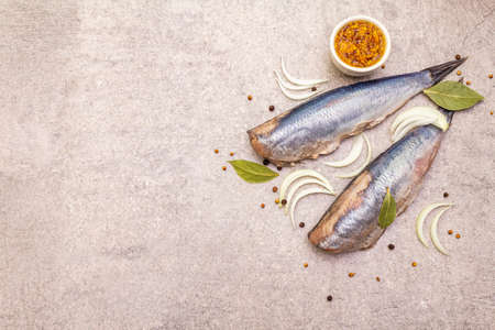 Traditional Norwegian herring "Matias Queen", whole carcasses. Ingredient for smorrebrod, snacks, antipasti. With sliced onion, black pepper, coriander. On stone background, top view, copy spaceの写真素材