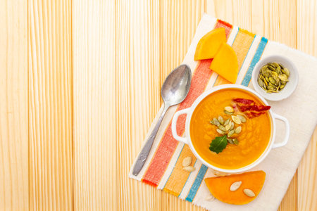 Pumpkin cream soup. White ceramic bowl with fresh pumpkin, dry pumpkin seeds, smoked bacon, herb. With vintage linen cloth (napkin) on wooden background, top view.の写真素材