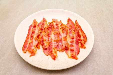 Smoked fried bacon slices. Stripes in round ceramic plate on stone background, close upの写真素材