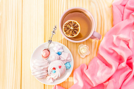 Romantic sweet breakfast concept. Green tea, lemon, meringue (cake). On wooden background with pink...