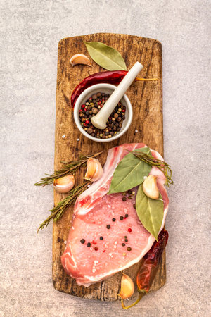 Raw pork steak with spices and dried herbs on vintage wooden board. Salt, garlic, hot pepper,...