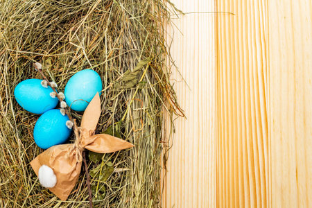 Easter eggs concept in a nest on hay with willow seals and paper bunny gift on wooden table...
