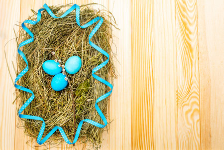 Easter eggs concept in a nest on hay with willow seals and blue polka dot ribbon on wooden table...