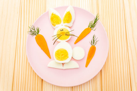 Easter bunny (rabbit) eggs children (kids) food concept. With carrot on rosy (pink) plate. Wooden...