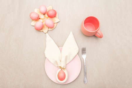 Easter bunny (rabbit) egg concept, table arrangement decoration. Pink (rosy) eggs with plate, fork,...