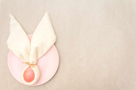 Easter bunny (rabbit) egg concept, table arrangement decoration. Pink (rosy) eggs with plate, cloth vintage linen napkin on a stone background, top view.の写真素材