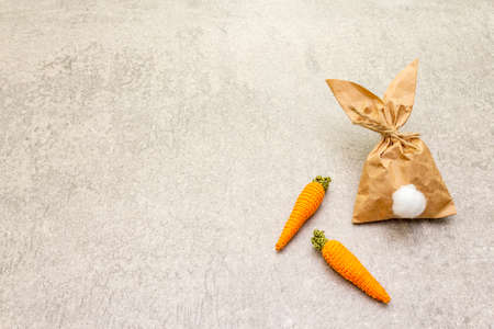Easter bunny (rabbit) paper gift wrapping with knitted carrots idea. Handicraft (homemade) concept for children (kids). On stone background.の写真素材