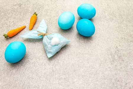 Easter bunny (rabbit) paper gift egg wrapping with knitted carrots idea. Handicraft (homemade) concept for children (kids). On stone background.の写真素材