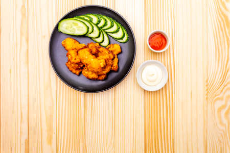 Chicken fried (nuggets) homemade on black plate with cucumber and two sauces - mayonnaise and hot spicy sauce. On wooden background, top view.の写真素材