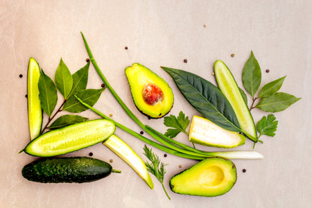 Green vegetables and herbs cooking background. Avocado, avocado leaf, bay leaf, cucumber, zucchini,...