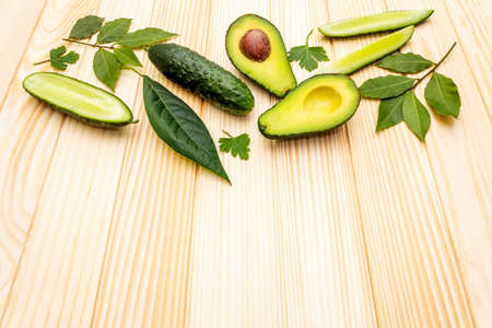 Green vegetables and herbs cooking background. Avocado, avocado leaf, bay leaf, cucumber, parsley. On a wooden background, flat lay.の写真素材