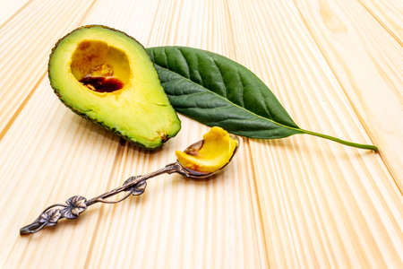 Avocado, cut in half and avocado leaf. Silver spoon with soy sauce. Cooking background. On the...