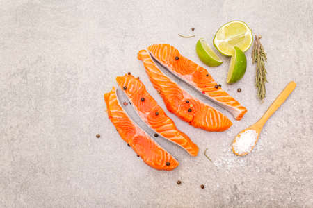 Raw trout (salmon) piece with lime, rosemary, sea salt and pepper mix. Fish on a stone background, top viewの写真素材