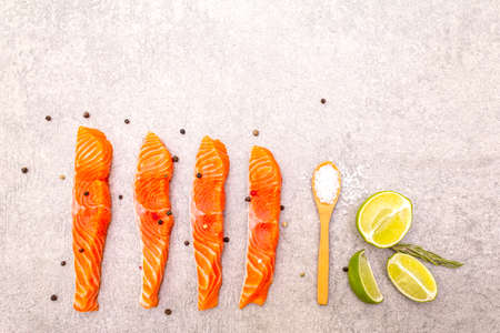 Raw trout (salmon) piece with lime, rosemary, sea salt and pepper mix. Fish on a stone background, top viewの写真素材