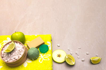 Spa concept, natural ingredients. Bath towel, sea salt with lime, apple, olive and mint soap, sponge. On a stone background.の写真素材